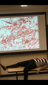 Woman lying on a table with a projection of blood spatter in the background.