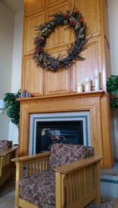 Armchairs in front of a fireplace with a wreath mounted on the wooden wall.
