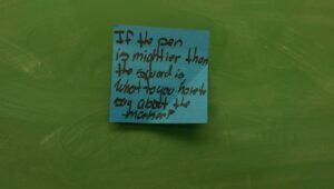 Green chalkboard with blue Post-It reading "If the pen is mightier than the sword, what to [sic] you have to say about the marker?"