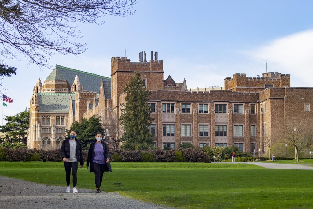 Two masked students walking on a university campus.