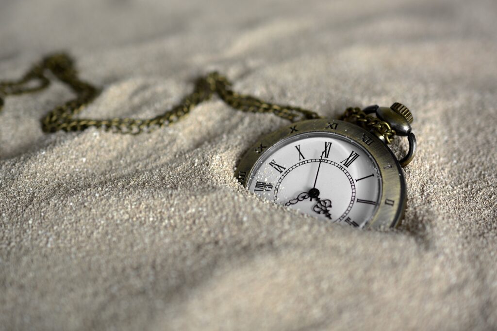 Pocket watch on a chain partly submerged in sand.
