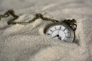 Pocket watch on a chain partly submerged in sand.